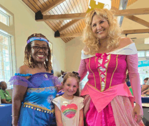 A princess in blue and a princess in pink stand with a young child.